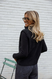 Gilet sans manches boutonné noir porté par une femme, vue de profil, mur blanc, cheveux blonds