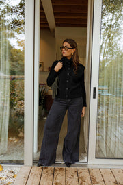 Gilet sans manches boutonné noir porté par une femme, vue de face, porte vitrée, pantalon gris