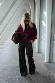 Gilet doux chaud à boutons bordeaux porté par une femme, vue de face, architecture blanche, sac marron