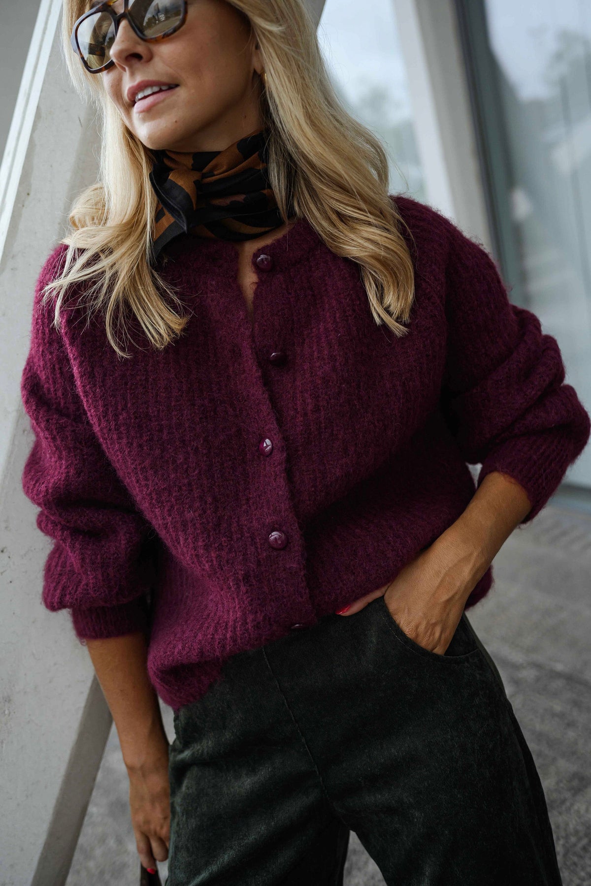 Gilet doux chaud à boutons bordeaux porté par une femme, vue rapprochée, lunettes de soleil, pantalon noir
