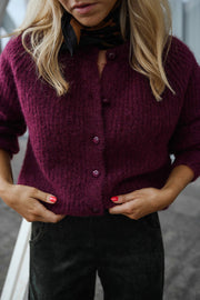 Gilet doux chaud à boutons bordeaux porté par une femme, vue rapprochée, mains sur les hanches, pantalon noir