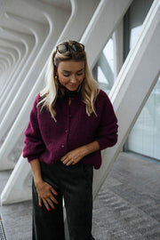 Gilet doux chaud à boutons bordeaux porté par une femme, vue de face, piliers blancs, lunettes sur la tête
