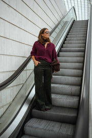 Gilet doux chaud à boutons bordeaux porté par une femme, vue de face, escalier mécanique, pantalon noir