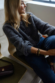 Gilet boutonné à col rond gris porté par une femme, assise, fauteuil beige, jean bleu
