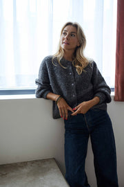 Gilet boutonné à col rond gris porté par une femme, vue de face, fenêtre, jean bleu