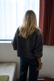 Gilet boutonné à col rond gris porté par une femme, vue de dos, rideau rouge, cheveux blonds