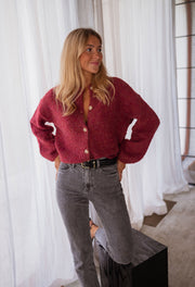 Gilet chiné boutonné bordeaux porté par une femme, vue de face, mains sur les hanches, jean gris