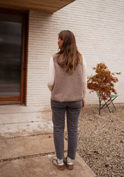 Gilet effet mouton et daim taupe porté par une femme, vue de dos, mur blanc, jean gris