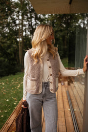 Gilet effet mouton et daim taupe porté par une femme, vue de trois-quarts, terrasse en bois, sac