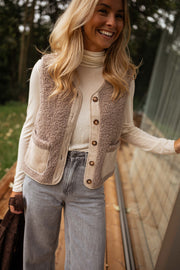Gilet effet mouton et daim taupe porté par une femme, vue de face, col roulé blanc, gilet
