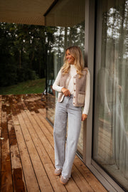 Gilet effet mouton et daim taupe porté par une femme, silhouette entière, baie vitrée, jean