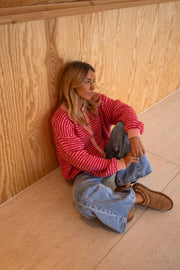 Gilet rayé à col rond porté par une femme, assise, parquet, mur en bois