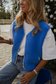 Gilet à bordures fleuries bleu porté par une femme, vue rapprochée, t-shirt blanc, jean clair