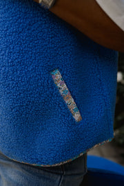 Gilet à bordures fleuries bleu porté par une femme, gros plan de la bordure fleurie