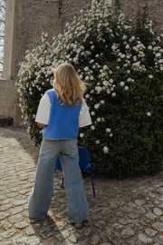Gilet à bordures fleuries bleu porté par une femme, vue de dos, jean, buisson fleuri