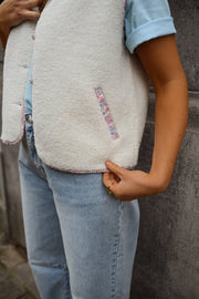 Gilet à bordures fleuries écru porté par une femme, gros plan de la bordure du gilet, jean clair