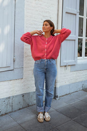 Gilet doux légèrement loose framboise porté par une femme, vue de face, volets bleus, bras écartés
