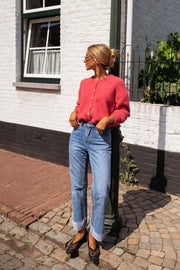 Gilet doux légèrement loose framboise porté par une femme, silhouette entière, rue pavée, volets