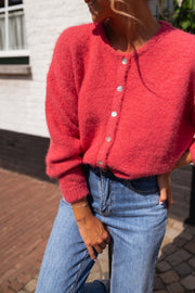 Gilet doux légèrement loose framboise porté par une femme, vue rapprochée, boutons nacrés, manches