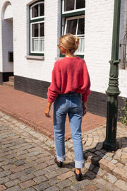 Gilet doux légèrement loose framboise porté par une femme, vue de dos, rue pavée, jean