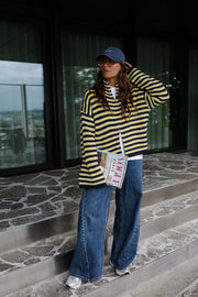 Gilet rayé à double zip porté par une femme, silhouette entière, casquette, sur un sol en pierre