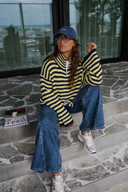 Gilet rayé à double zip porté par une femme, assise, sur des marches, casquette