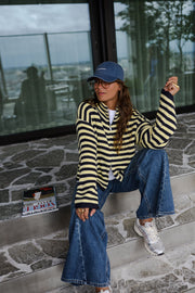 Gilet rayé à double zip porté par une femme, assise, sur des marches, casquette, magazine
