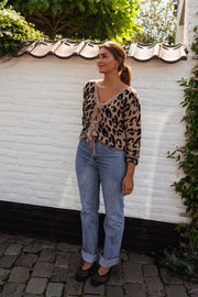 Gilet léopard à liens noués porté par une femme, silhouette entière, mur blanc, jean