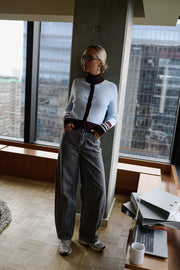 Gilet torsadé à col montant porté par une femme, silhouette entière, près d'une fenêtre