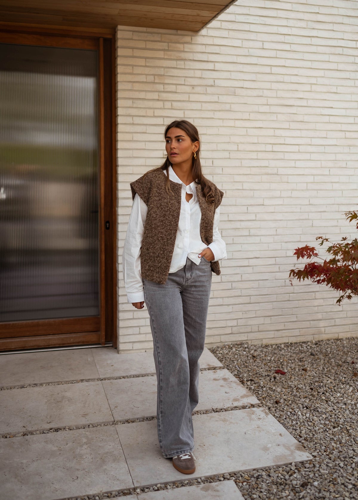 Gilet sans manches épais chocolat porté par une femme, silhouette entière, porte, chemise blanche