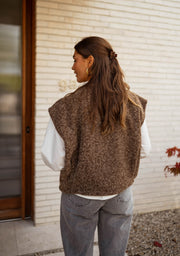 Gilet sans manches épais chocolat porté par une femme, vue de dos, porte, cheveux longs
