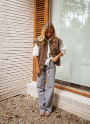 Gilet sans manches épais chocolat porté par une femme, silhouette entière, fenêtre, volets