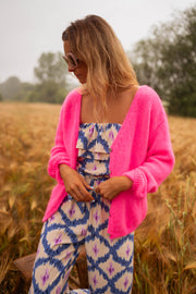 Gilet à col V boutonné rose porté par une femme, vue de face, champ de blé, combinaison bleue
