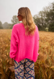 Gilet à col V boutonné rose porté par une femme, vue de dos, champ de blé, pantalon à motifs