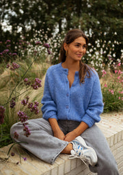 Gilet doux boutonné bleu porté par une femme, assise, muret, fleurs
