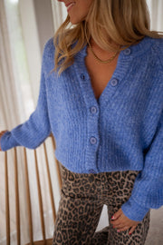 Gilet doux boutonné bleu porté par une femme, vue rapprochée, boutons, pantalon léopard