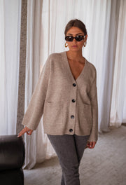 Gilet long droit à poches beige porté par une femme, vue de face, lunettes, canapé noir