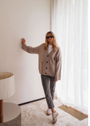 Gilet long droit à poches beige porté par une femme, vue de profil, mur blanc, bras tendu
