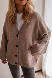 Gilet long droit à poches beige porté par une femme, vue rapprochée, poches, pull blanc