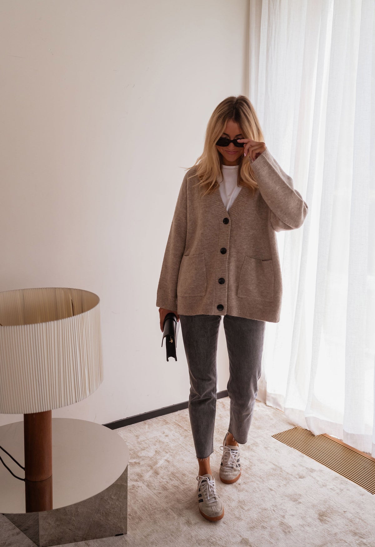 Gilet long droit à poches beige porté par une femme, silhouette entière, lampe, jean gris