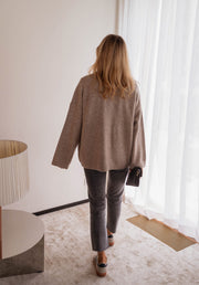 Gilet long droit à poches beige porté par une femme, vue de dos, rideaux, jean gris