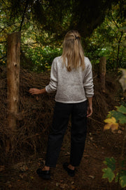Gilet boutonné à poches beige porté par une femme, vue de dos, forêt, pantalon noir