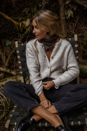 Gilet boutonné à poches beige porté par une femme, assise, chaise en bois, jambes croisées