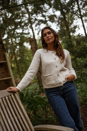 Gilet boutonné à poches beige porté par une femme, vue de face, chaise en bois, jean bleu