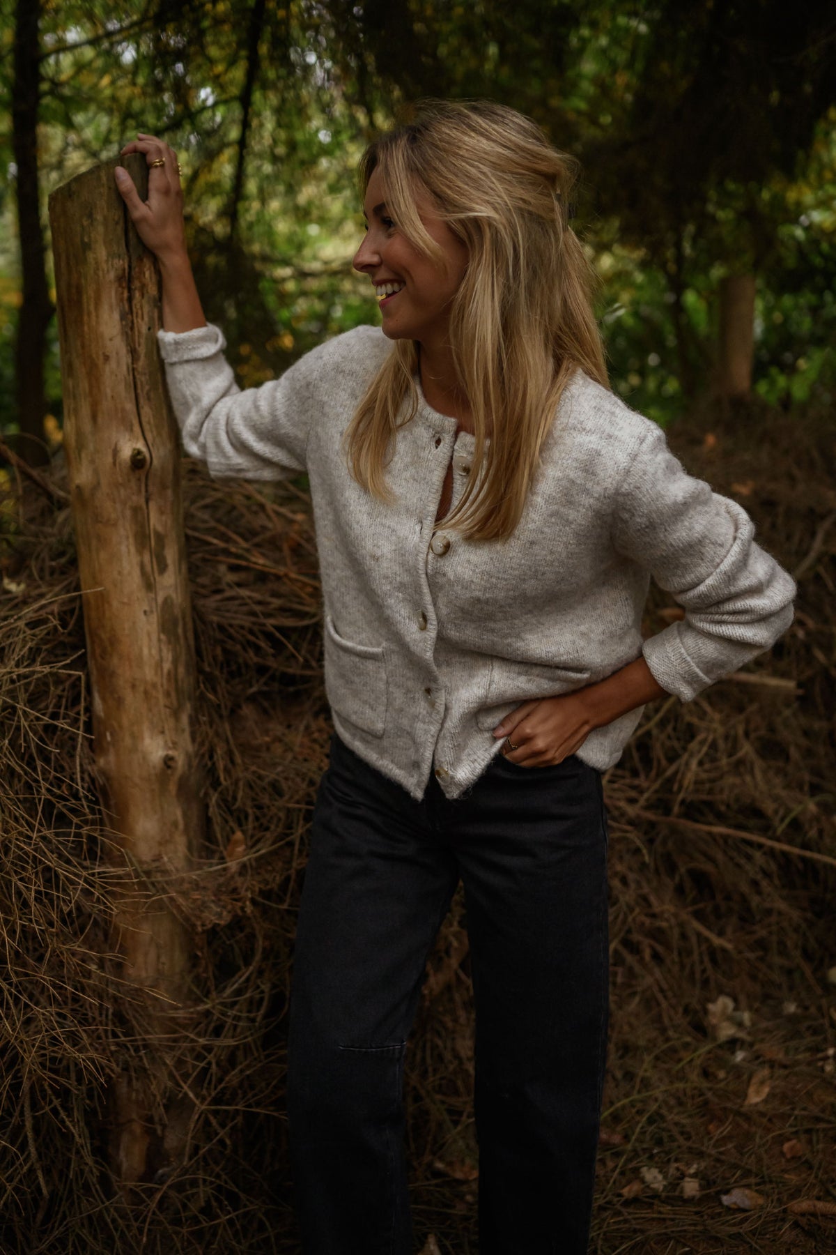 Gilet boutonné à poches beige porté par une femme, vue de face, tronc d'arbre, pantalon noir