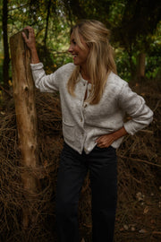 Gilet boutonné à poches beige porté par une femme, vue de face, tronc d'arbre, pantalon noir