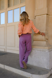 Gilet doux légèrement ample porté par une femme, silhouette entière, pantalon violet, devant une fenêtre
