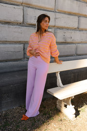 Gilet doux légèrement ample porté par une femme, silhouette entière, pantalon violet, sur un banc