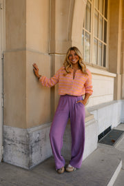 Gilet doux légèrement ample porté par une femme, silhouette entière, pantalon violet, adossée à un mur