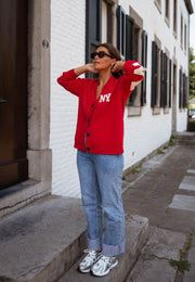 Gilet ample boutonné rouge porté par une femme, vue de face, lunettes, jean